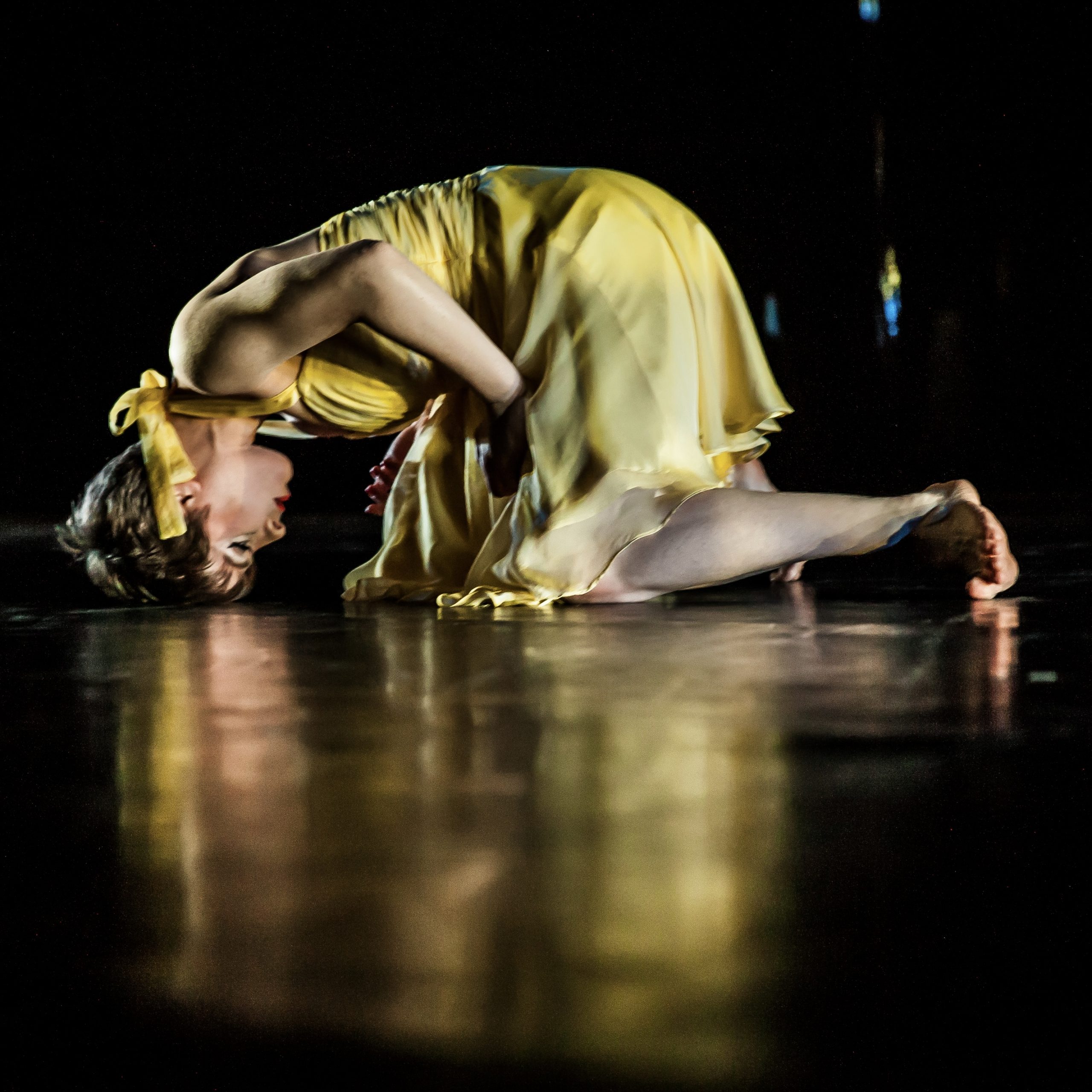 Merryn is kneeling in a yellow dress, head bowed to the floor.